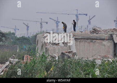 Two workers demolish a building as tower cranes build new housing in the background Stock Photo