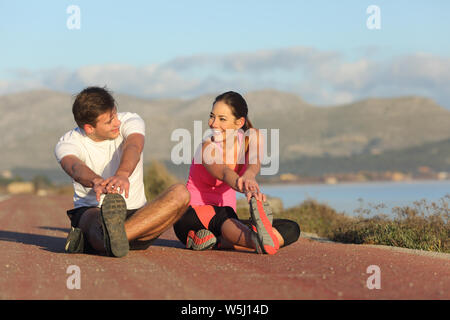 Couple of runners stretching legs after sport sitting on the road Stock Photo