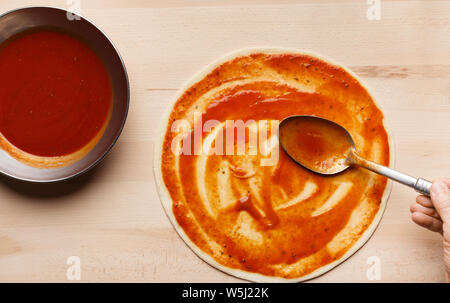 Chef spreading tomato sauce on pizza base Stock Photo