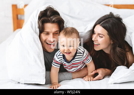 Cheerful parents playing with baby son in bed Stock Photo