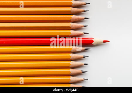 Red pencil standing between classic ones on white background
