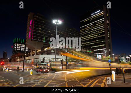 A Metrolink tram passes through Piccadilly Gardens in Manchester, UK at night. Stock Photo