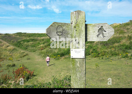 A walker on the Pembrokeshire Coast Path passes a signpost for the coastal path between Solva and St David's in summer July 2019 Stock Photo