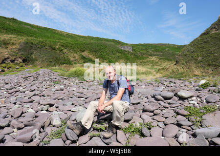 Middle aged man walker resting on rocks along the Pembrokeshire Coast Path near Caefai Bay summer 2019 Stock Photo