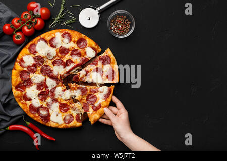 Woman taking slice of pepperoni pizza on black table Stock Photo