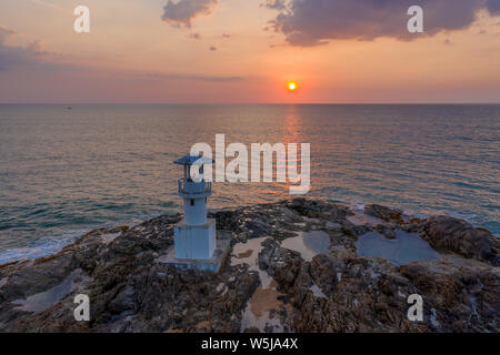 Aerial drone view of a tropical sunset behind a small lighthouse on a rocky island Stock Photo