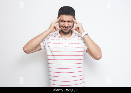 headache or confution. Portrait of confused handsome bearded young man in striped t-shirt standing, holding his painful head or thinking. indoor studi Stock Photo