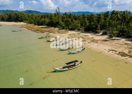 Aerial view of traditional wooden Longtail boats moored off a quiet, tropical sandy beach