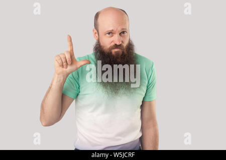 I am loser. Portrait of sad middle aged bald man with long beard in light green t-shirt standing with loser gesture and looking with failure face. ind Stock Photo
