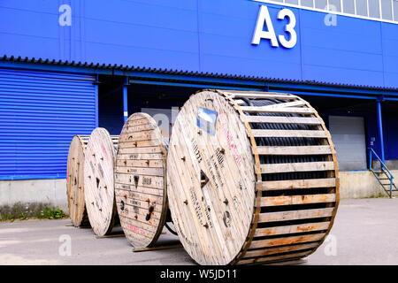 A thick electrical cable on wooden spools. Coils are marked. Warehouse. Storage terminal, blue building Stock Photo