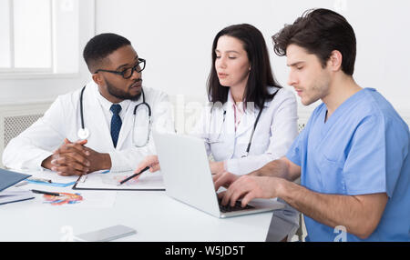 Young medical team discussing reports, using laptop Stock Photo