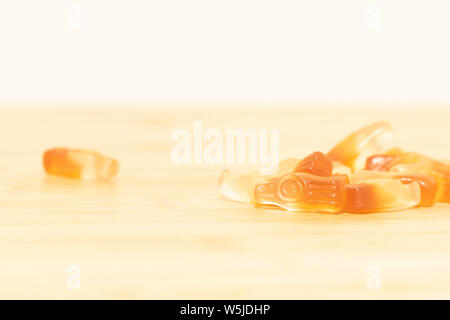 A very light and dreamy portrait of some cola bottle shaped candy on a wooden table. The sweets have the same colors as a half full bottle of cola. Stock Photo