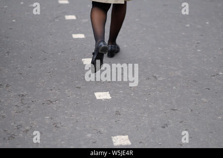 The legs of a woman walking along the dividing strip of an asphalt road