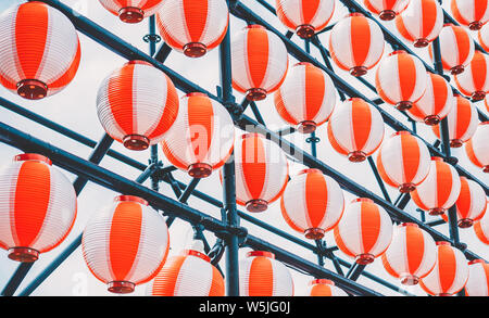 Many paper red-white oriental paper lanterns hanging in a row on blue sky background Stock Photo