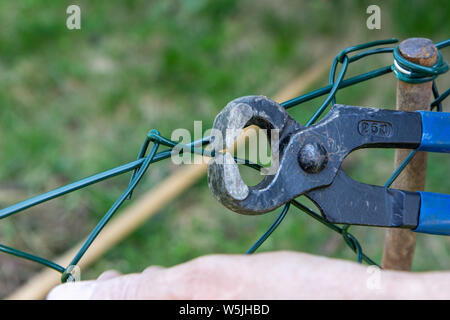 a man repairing a metal wire fence with pliers Stock Photo
