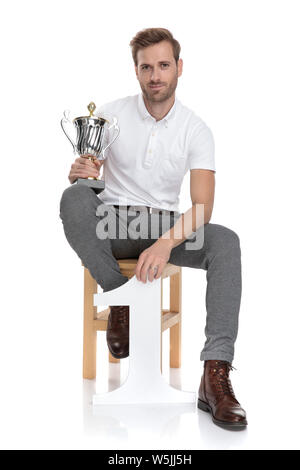 happy young casual man sitting and holds a trophy and number one on white background Stock Photo