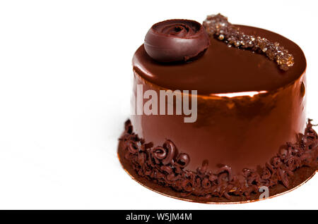 A delicious chocolate cake with chocolate pieces lies on a wooden stand next to a white cup, which stands on a white wooden table Stock Photo