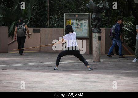 Young woman practicing with kung fu stick at Kung Fu Court of Kowloon Park, Hong Kong Stock Photo