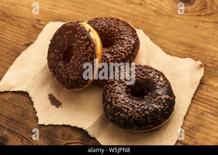 Three sweet doughnuts with chocolate cream and crumbs on rustic wooden table Stock Photo