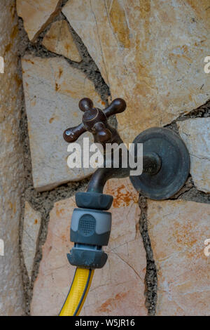 an outside tap or faucet with a yellow hosepipe attached for watering the garden. Stock Photo