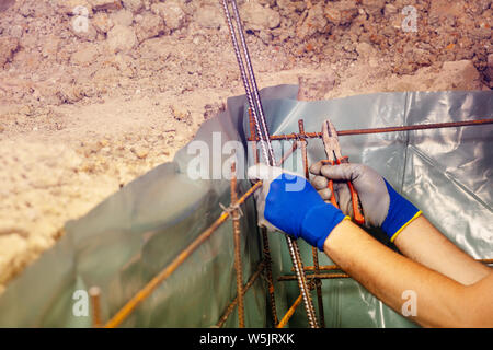 Closeup of man knitting metal rods for concrete framework holding bars and wearing gloves Stock Photo