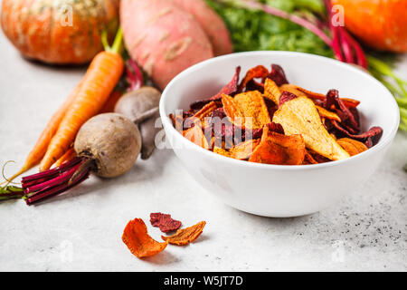 Bowl of healthy vegetable chips from beets, sweet potatoes and carrots with ingredients on a white background. Stock Photo