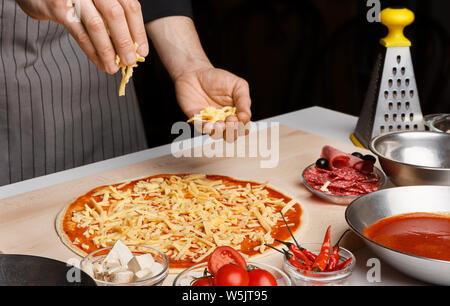 Chef preparing pizza, adding cheese to pizza base Stock Photo