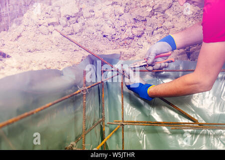 Closeup of man knitting metal rods with pillars for concrete framework holding bars and wearing gloves Stock Photo
