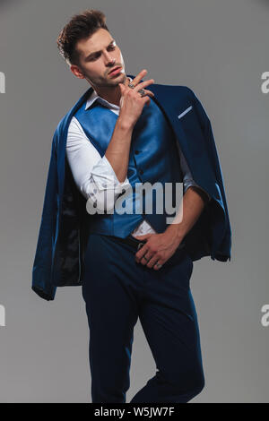 portrait of arrogant young man wearing blue suit looking down to side while standing on light grey background Stock Photo
