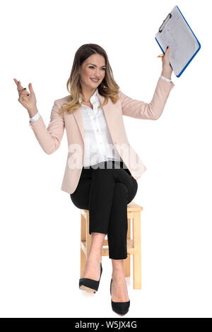 curious seated smart casual woman holds clipboard in the air on white background and looks to side Stock Photo