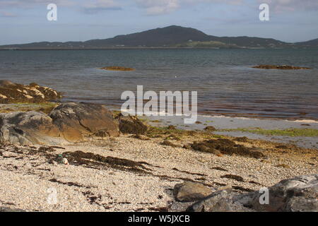 View from East Kilbride, South Uist, over the sea to Eriskay with a rocky beach in the foreground Stock Photo