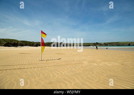 Red and yellow flags flying on a sunny day at a sandy cornish beach Stock Photo