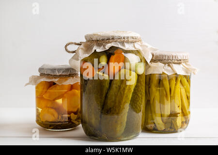 Jars of pickled vegetables: cucumbers, tomatoes, eggplants on rustic wooden background. Marinated and canned food. Stock Photo
