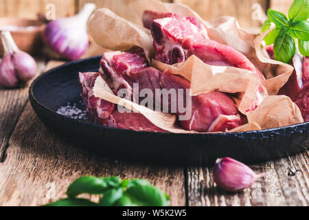 Raw veal steaks with cooking  ingredients, sea salt, garlic, basil herbs ready to cook, preparing food, rural wooden table, close up, selective focus Stock Photo