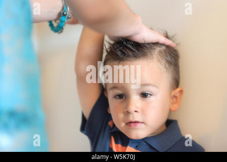 Mother measuring height of her son near white wall . Stock Photo