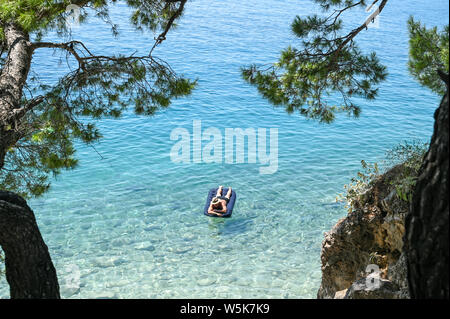 Unrecognizable tourist enjoys the beach at Brela. The Makarska riviera in Croatia is famous for its beautiful pebbly beaches and crystal clear water. Stock Photo