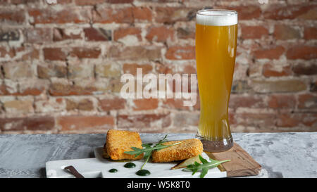 Glass of beer on the stone table and brick's background. Cold drink and meat snacks are prepared for a big friend's party. Concept of drinks, fun, food, celebrating, meeting, oktoberfest. Stock Photo