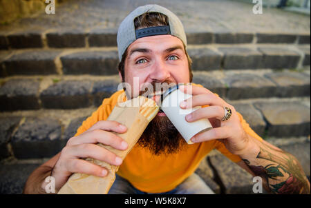 Unleashed appetite. Street food concept. Man bearded eat tasty sausage. Urban lifestyle nutrition. Junk food. Carefree hipster eat junk food while sit stairs. Guy eating hot dog. Snack for good mood. Stock Photo