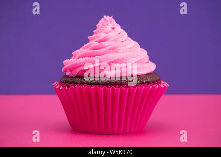 Single Pink Frosted Chocolate Cupcake on a Pink and Purple Surface Stock Photo