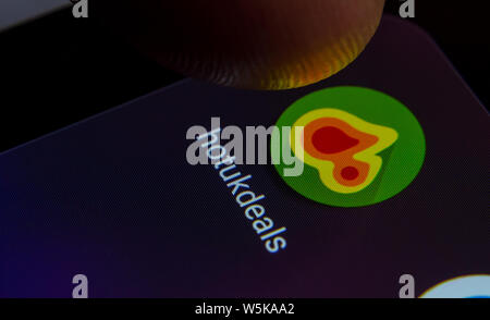 HotUkDeals app icon on the smartphone screen with visible pixels and the finger about to launch it. Stock Photo