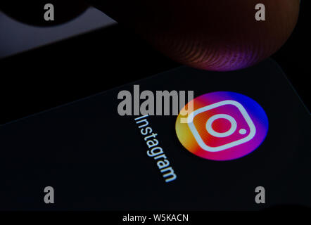 Instagram app icon on the smartphone screen with visible pixels and the finger about to launch it. Stock Photo
