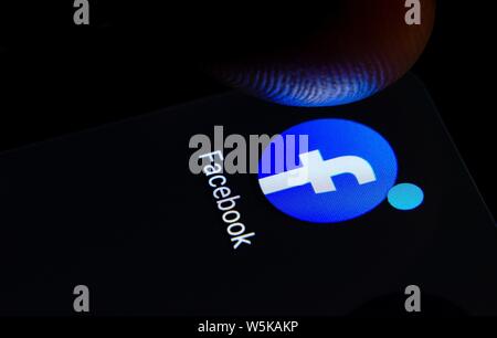 Facebook app icon on the smartphone screen with visible pixels and the finger about to launch it. Stock Photo