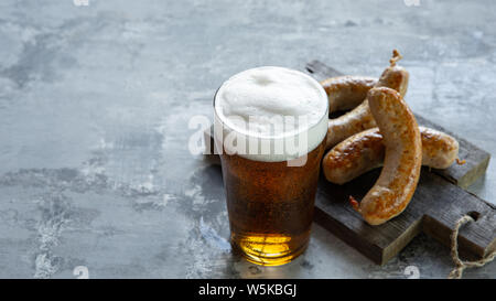Glass of beer with foam on top on white stone background. Cold alcohol drink and sausages are prepared for a big friend's party. Concept of drinks, fun, food, celebrating, meeting, oktoberfest. Stock Photo