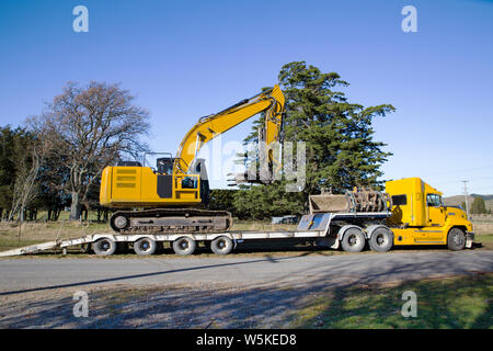 A large yellow digger is loaded onto a truck and tailer unit after completing a job in Canterbury, New Zealand Stock Photo