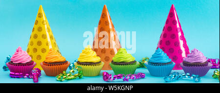 Rainbow Colored Frosted Chocolate Cupcakes on a Teal Background Stock Photo