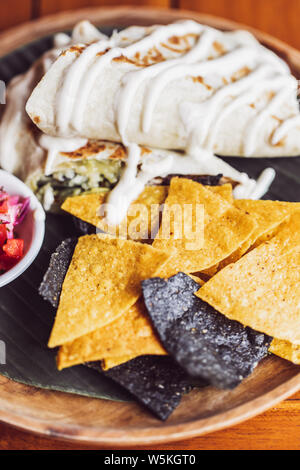 Yellow and black corn nacho chips garnished with guacamole, melted cheese on wooden plate. Traditional mexican food. Vertical photo. Stock Photo