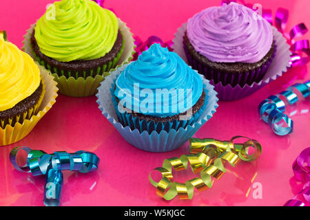 Rainbow Colored Frosted Chocolate Cupcakes on a Pink Background Stock Photo