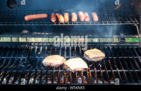 Hot dogs and cheeseburgers are cooking on a coal grill during a summer barbecue. Stock Photo