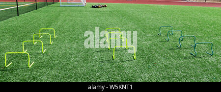 Green truf field is set up for agility and strength practice with rows of mini yellow banana hurdles and medicine balls. Stock Photo