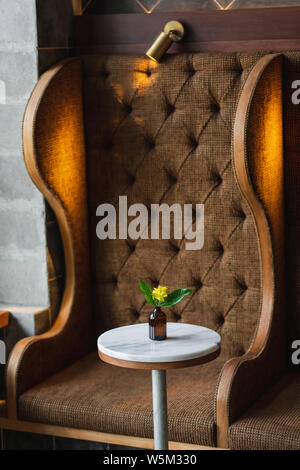 Small round marble table in cafe and bottle with yellow flower. Dark brown background, minimalist modern style Stock Photo